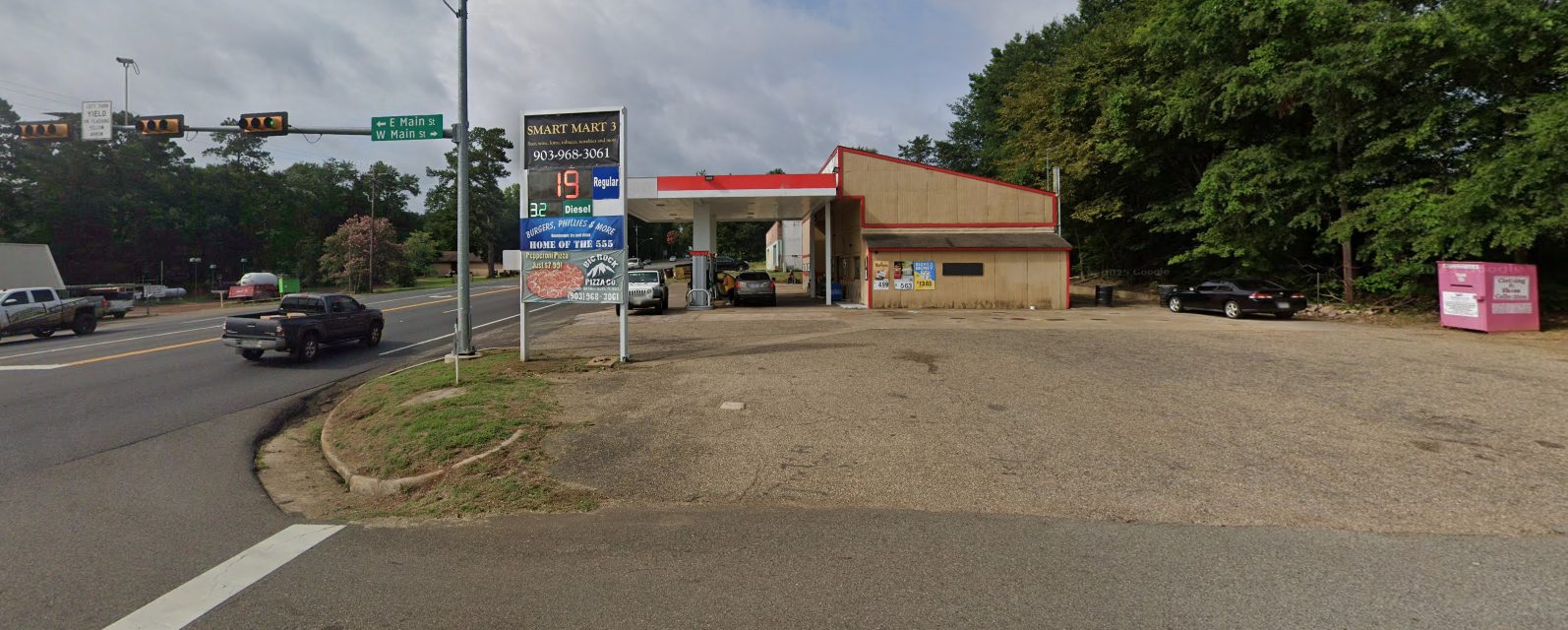 Corner signage with fuel pricing, deli, and pizza panels at the Main St intersection